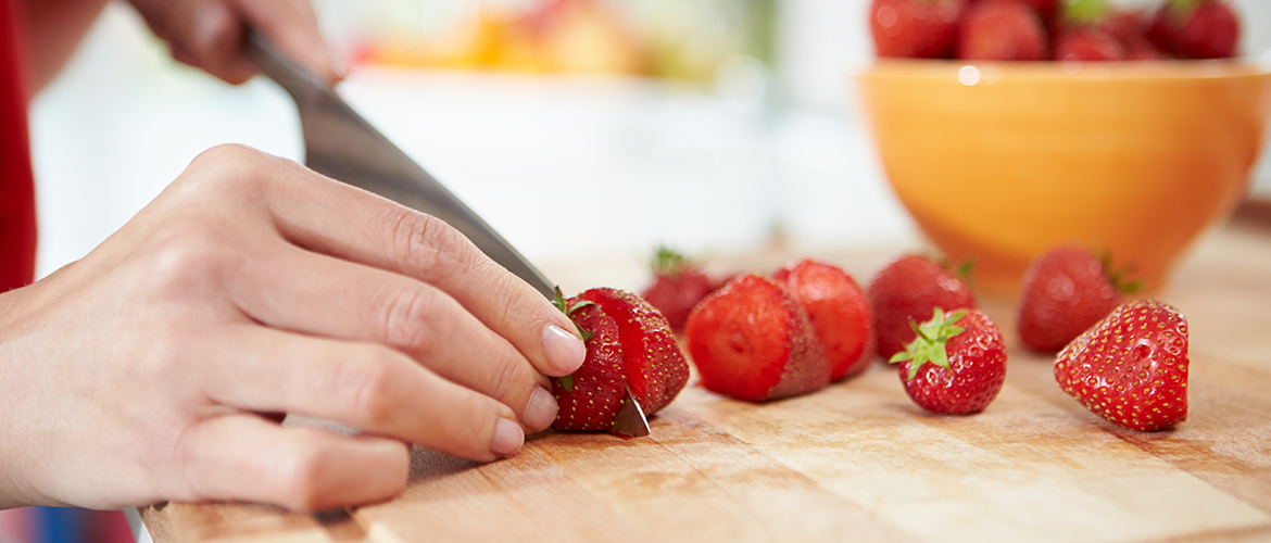 hand cutting a strawberry on a wooden cutting board