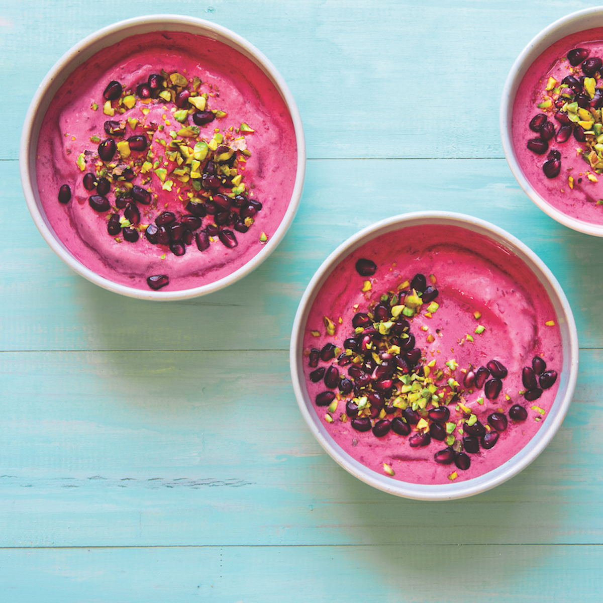 three pomegranate cherry smoothie bowls on a blue background