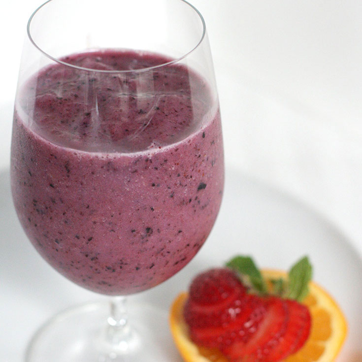 blue smoothie in a glass with a strawberry on the side
