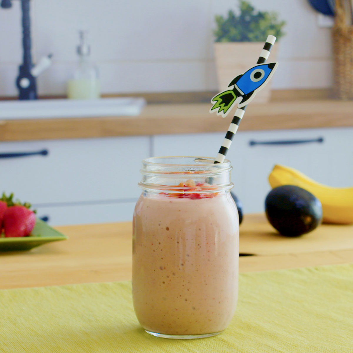 peanut butter and jelly smoothie with fun straw on a counter with banana, strawberries and avocado