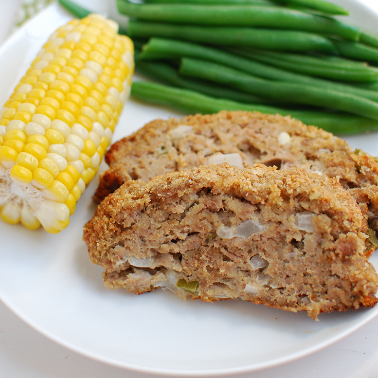 slices of meatloaf on a plate with corn on the cob and green beans